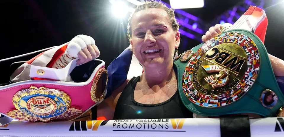 Boxeadora sosteniendo cinturones de campeona en el ring