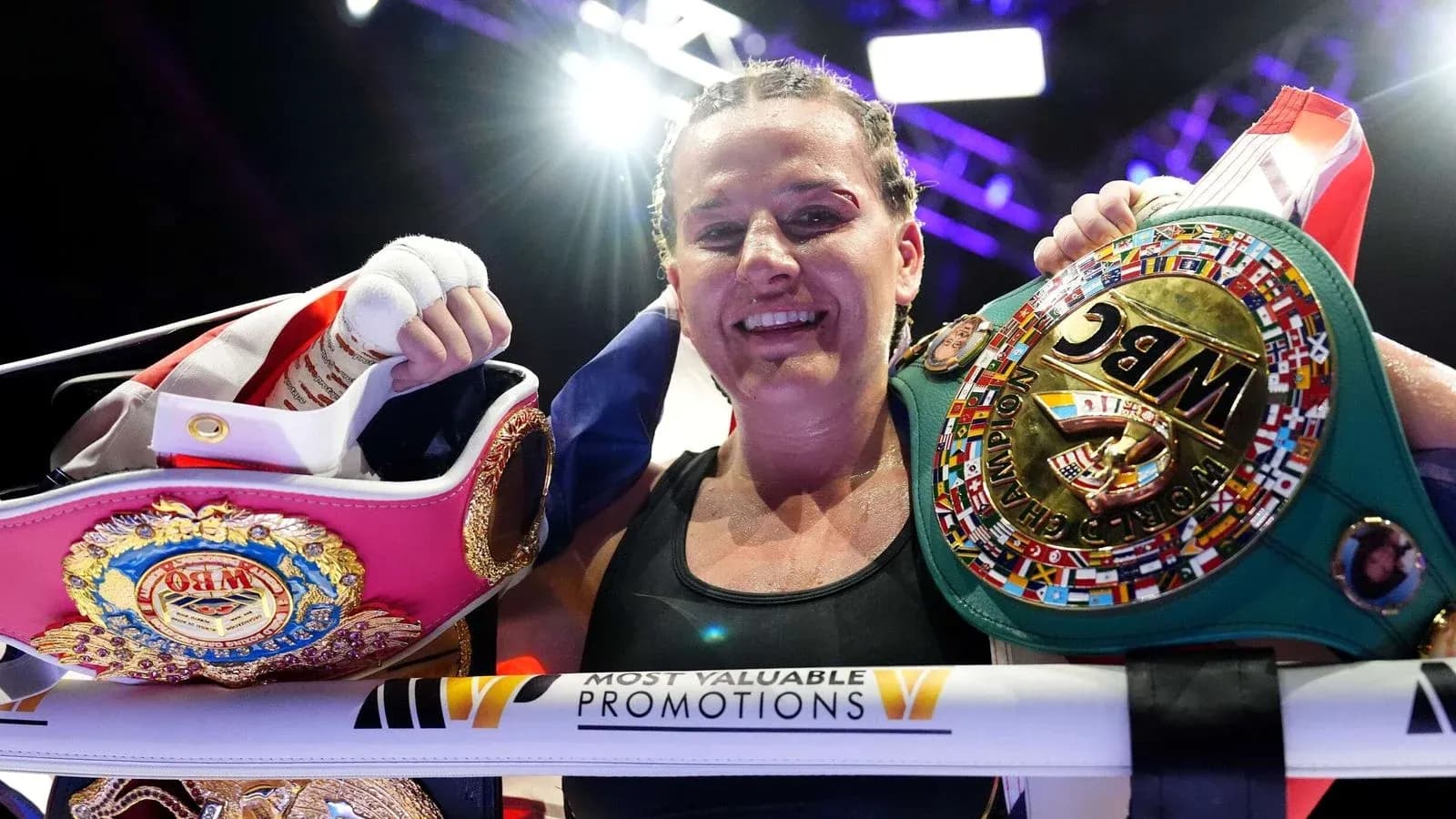 Boxeadora sosteniendo cinturones de campeona en el ring
