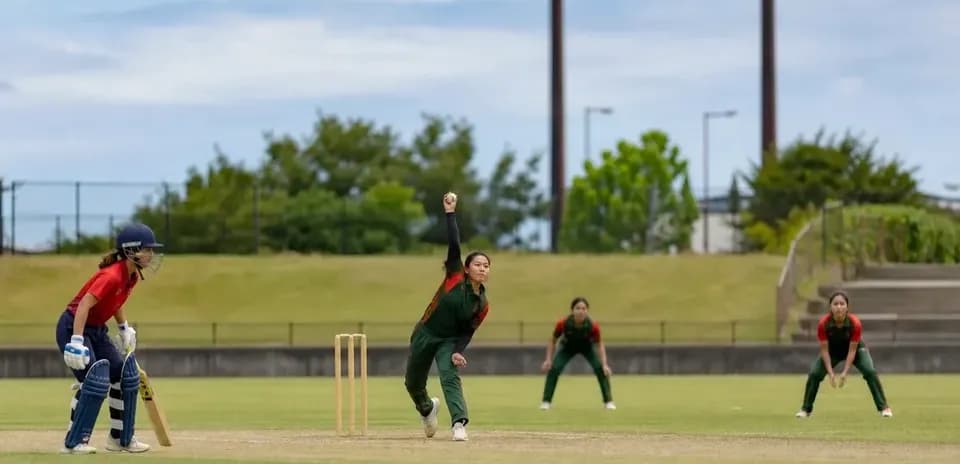 Jugadora lanzando en un partido de cricket femenino