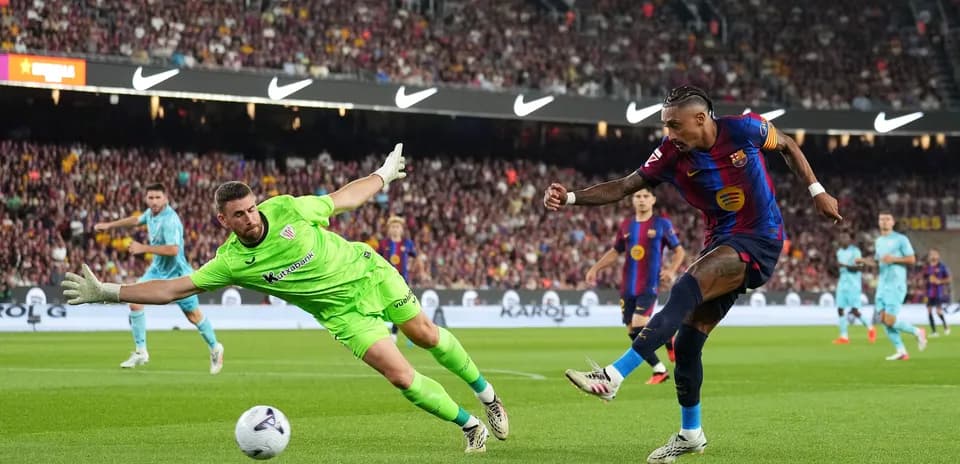 Jugador de Barcelona disparando mientras el portero intenta detenerlo
