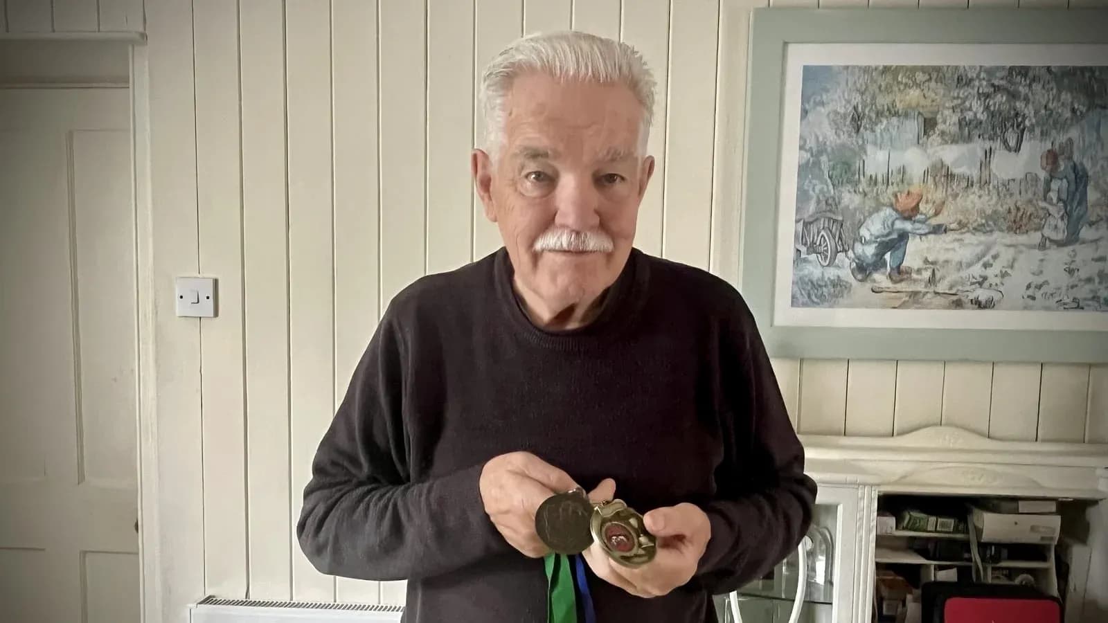 Hombre mayor sosteniendo medallas en casa
