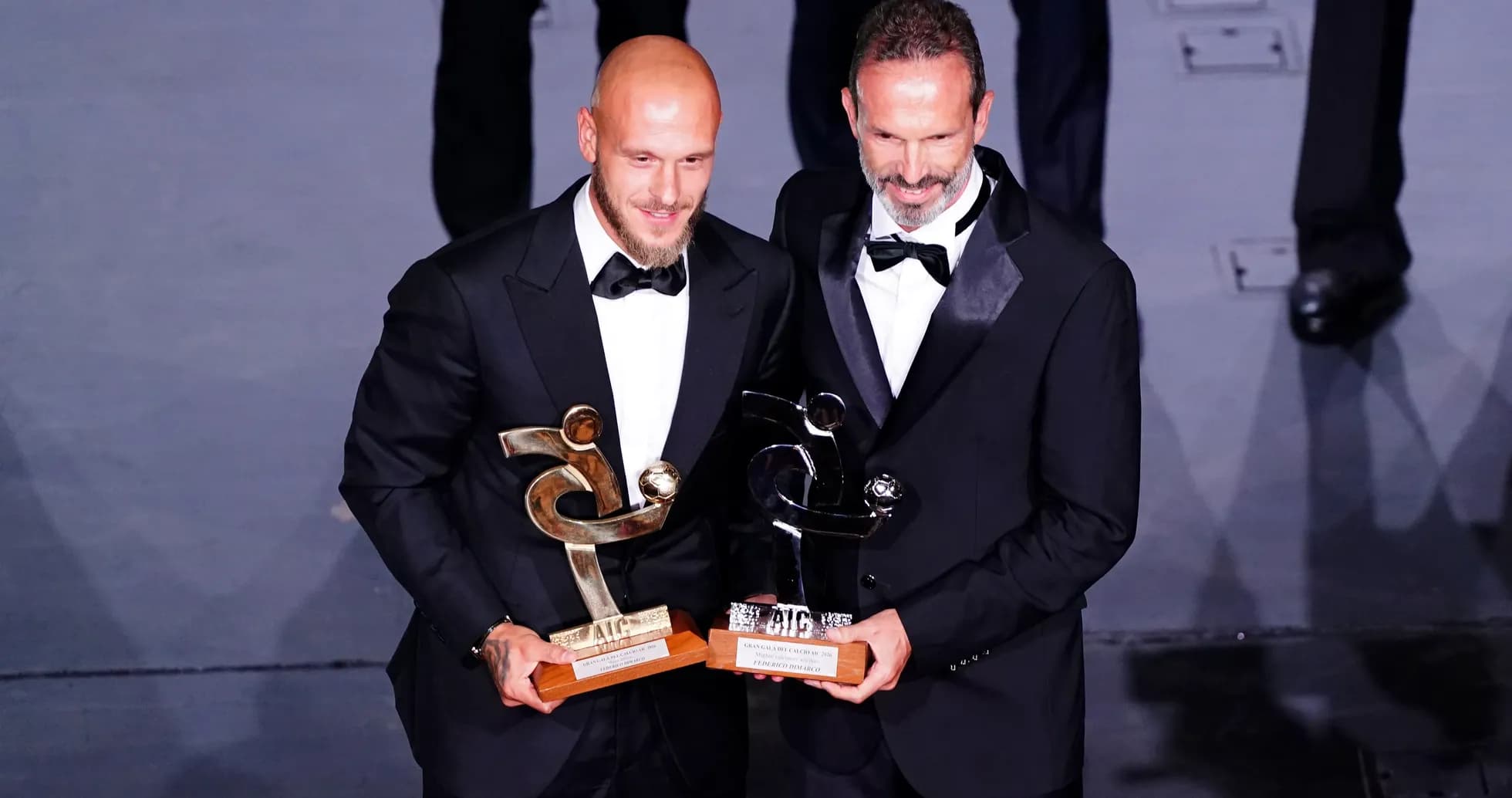 Dos hombres con trofeos en evento de premiación Dos hombres con trofeos en evento de premiación